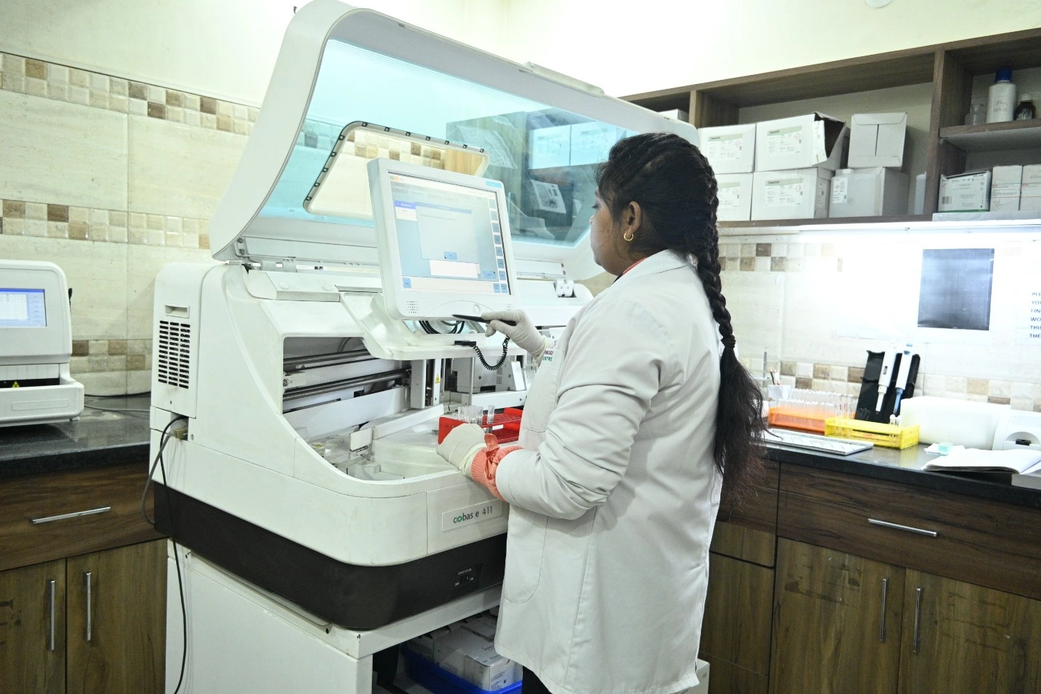 Laboratory technician operating a Cobas e 411 automated analyzer for clinical chemistry tests.